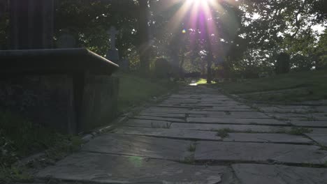 sunbeams over old churchyard path at sunset wide tilting shot