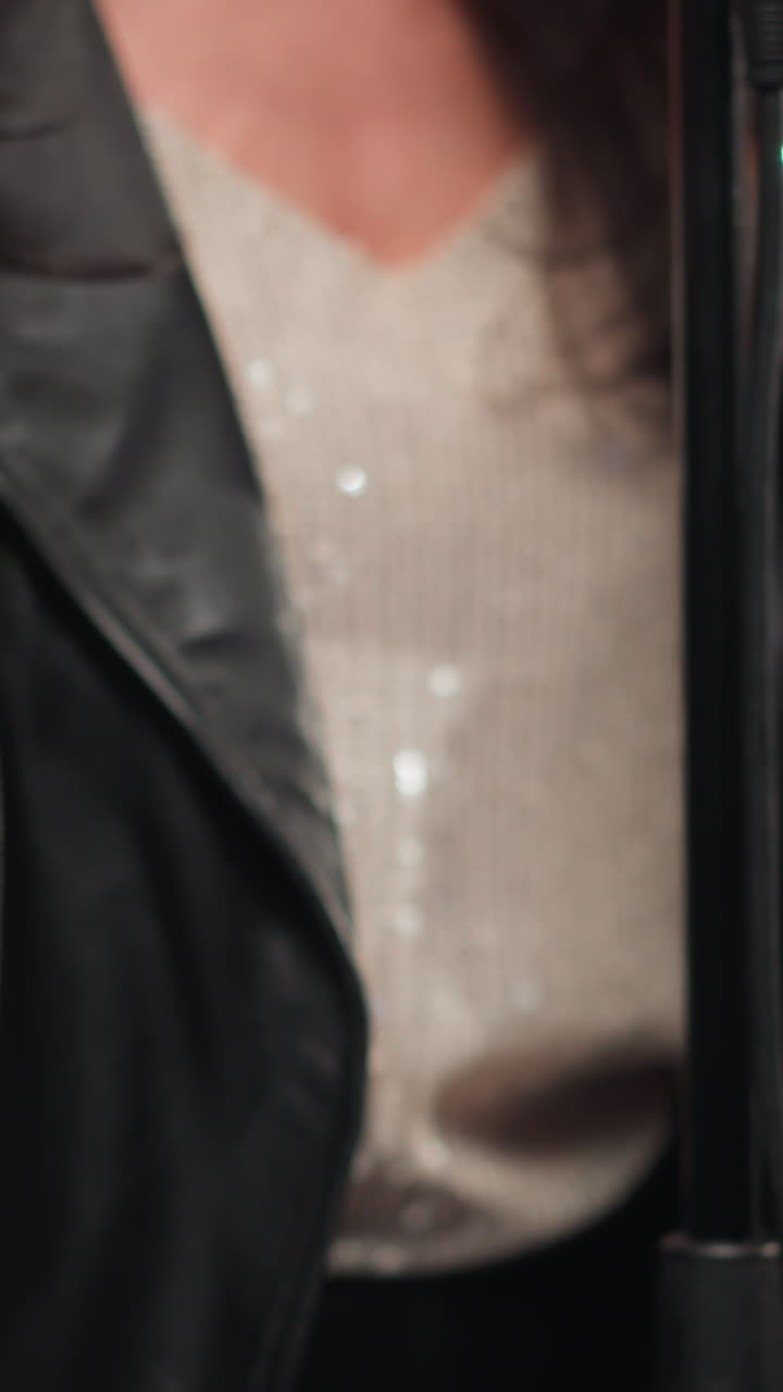 primer plano detallado de una vocalista femenina sin rostro con una chaqueta de cuero negra, manos plegadas, en un fondo gris minimalista