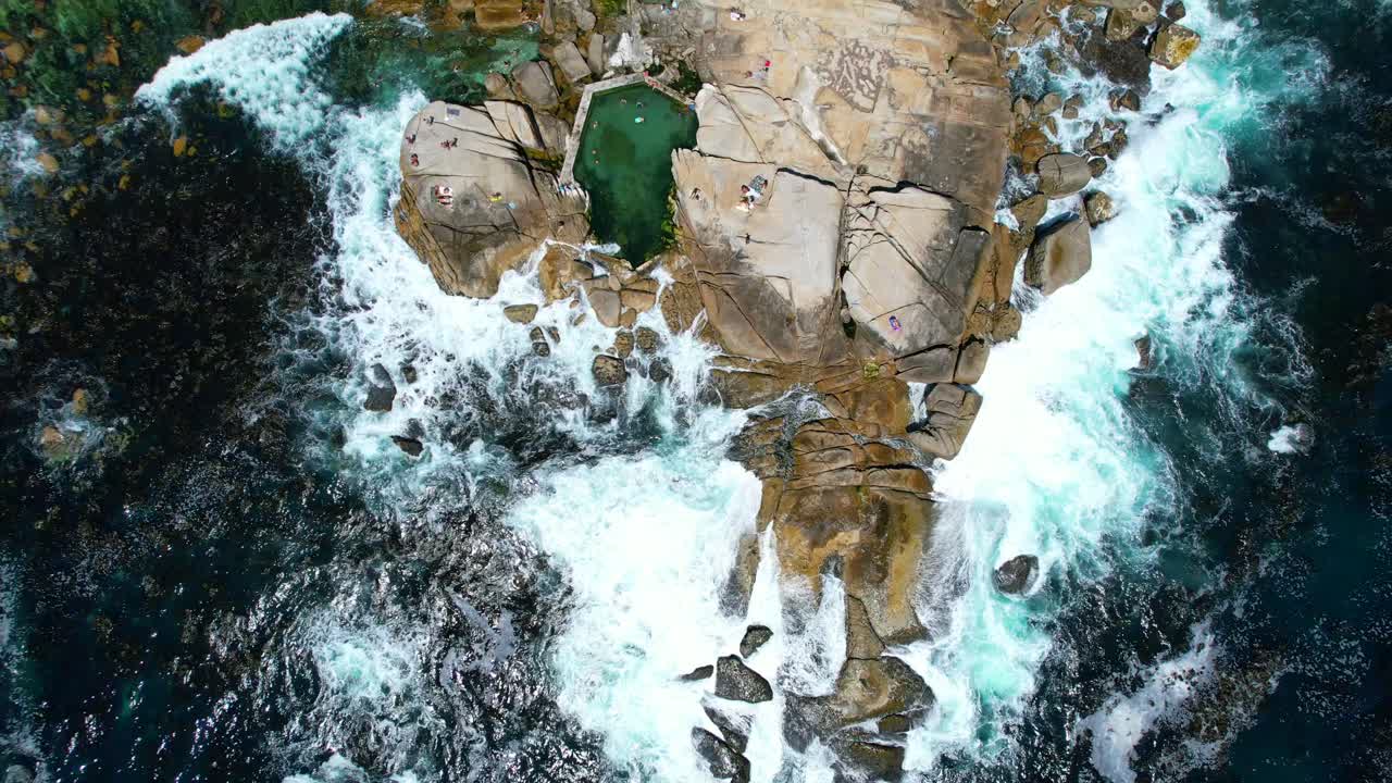 vista de arriba hacia abajo de la gente en la playa de rocas saunders mientras las olas chocan contra las rocas, antena