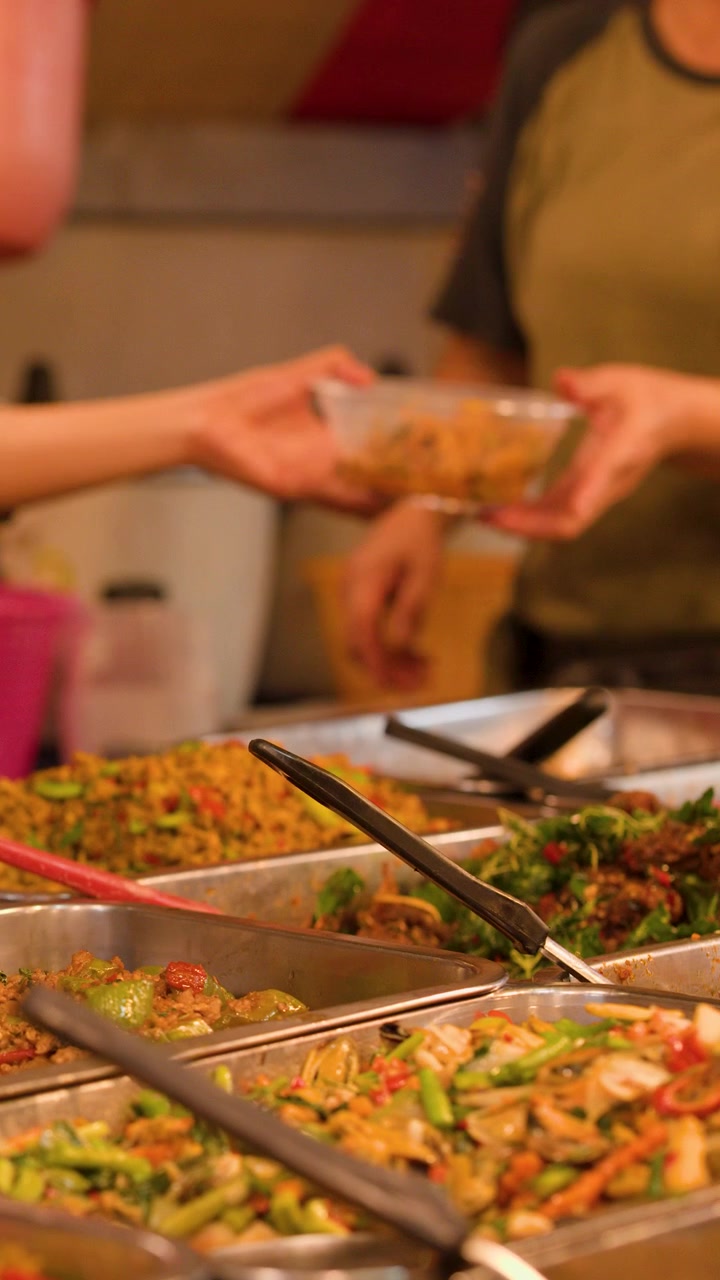 Primo piano di un venditore che serve curry da asporto in ciotole di plastica in un vivace mercato notturno all'aperto