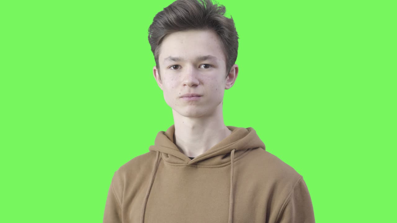 진지한 십대 남성의 클로즈업, 카메라를 바라보며 조용한 몸짓을 하고, 초록색 배경에 포즈를 취하는 갈색 백인 소년의 초상화, 비밀을 지키고, 소문, 라이프 스타일, 크로마키