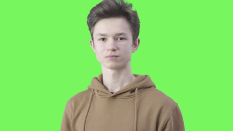 close-up of serious teenager making hush gesture and looking at camera. portrait of brunette caucasian boy posing at green background. keeping secrets, gossiping, lifestyle. chromakey.