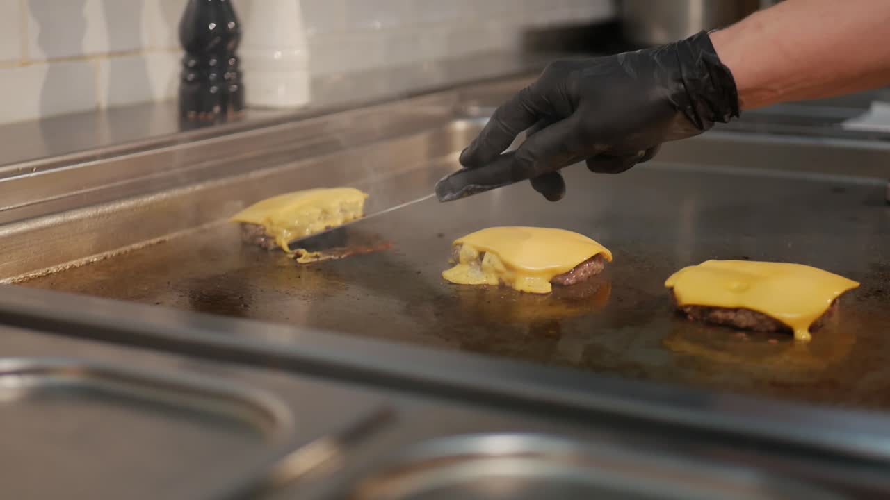 요리사는 뜨거운 난로에서 요리된 치즈버거 패티를 가져오고 정적 샷을 합니다.