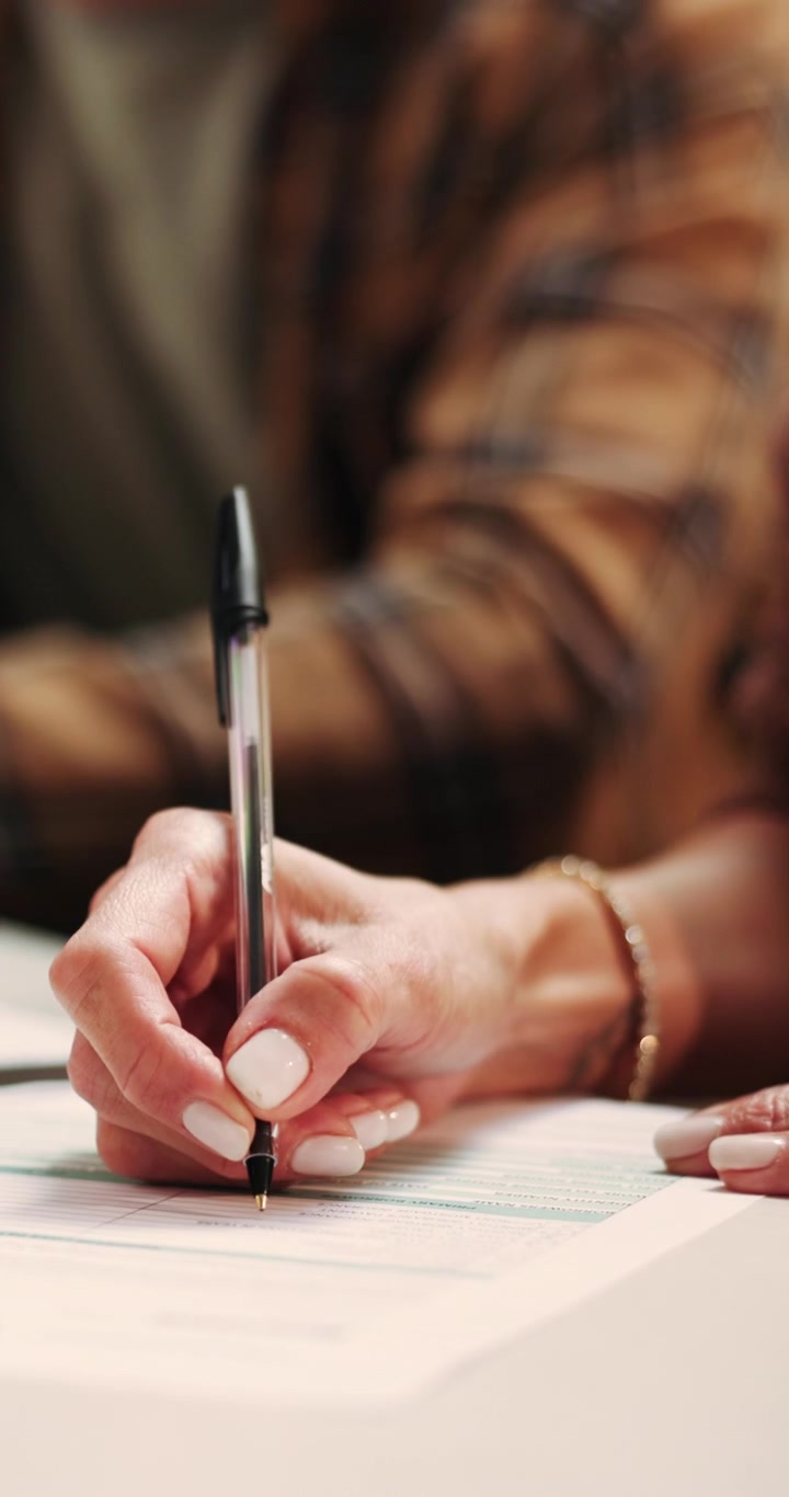 Close-up of Woman Signing a Document with Man Assisting