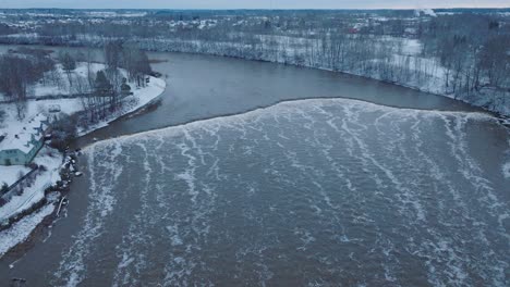 vista aérea de los rápidos del río venta durante la inundación de invierno, viejo puente de ladrillo rojo, kuldiga, letonia, día de invierno nublado, amplia toma de drone moviéndose hacia atrás