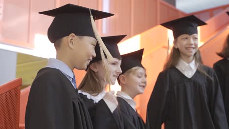 side view of happy kindergarten students in cap and gown dancing and having fun during the preschool graduation ceremony