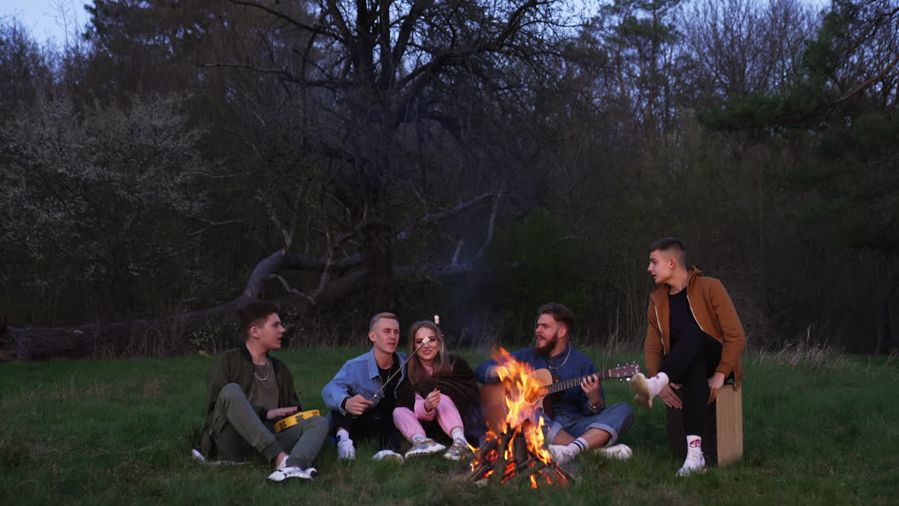 Friends having fun around a campfire at night in a forest