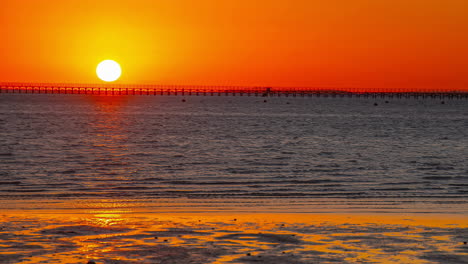 Impresionantes-Vistas-De-La-Playa-Con-El-Sol-Saliendo-En-El-Horizonte,-Gente-Calentándose-Junto-Al-Mar