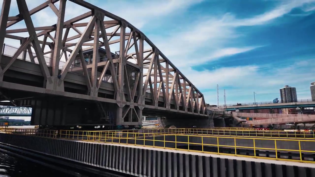 Moving boat passes beneath the Vernon Boulevard swing bridge and industrial waterfront on Newtown Creek in New York City, Speed Ramp