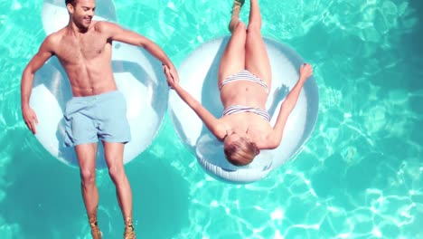 Attractive-couple-relaxing-on-lilos-in-pool