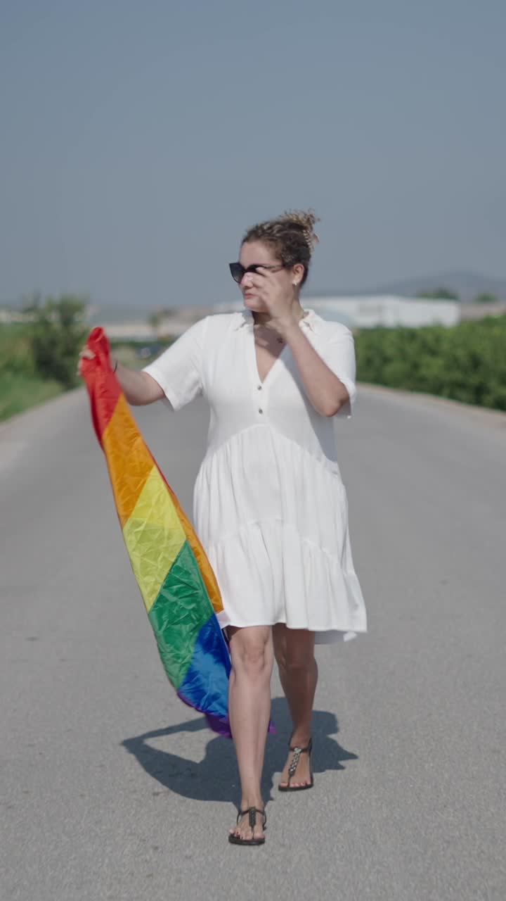 Woman walking on a road with a rainbow flag