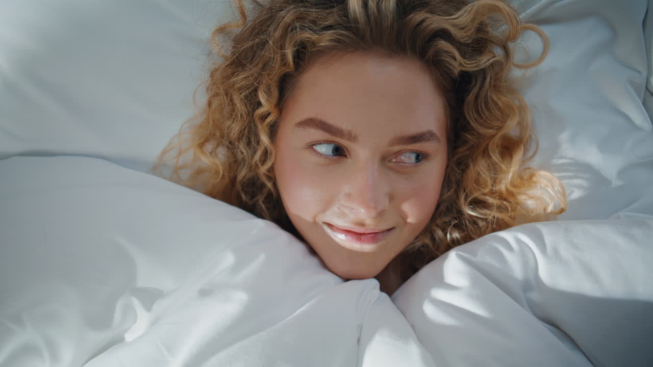 Relaxed girl lying bed hiding under blanket in morning. Closeup playful eyes