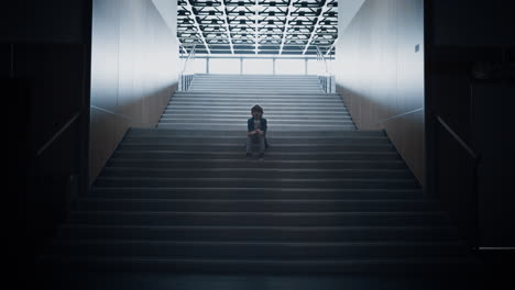 Lonely schoolchild sitting alone on school staircase closeup. Boy hide in hall.