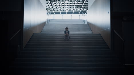 lonely schoolchild sitting alone on school staircase closeup. boy hide in hall.