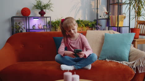 Child-toddler-hold-smartphone-watching-funny-cartoons,-chatting-with-friends-on-couch-alone-at-home