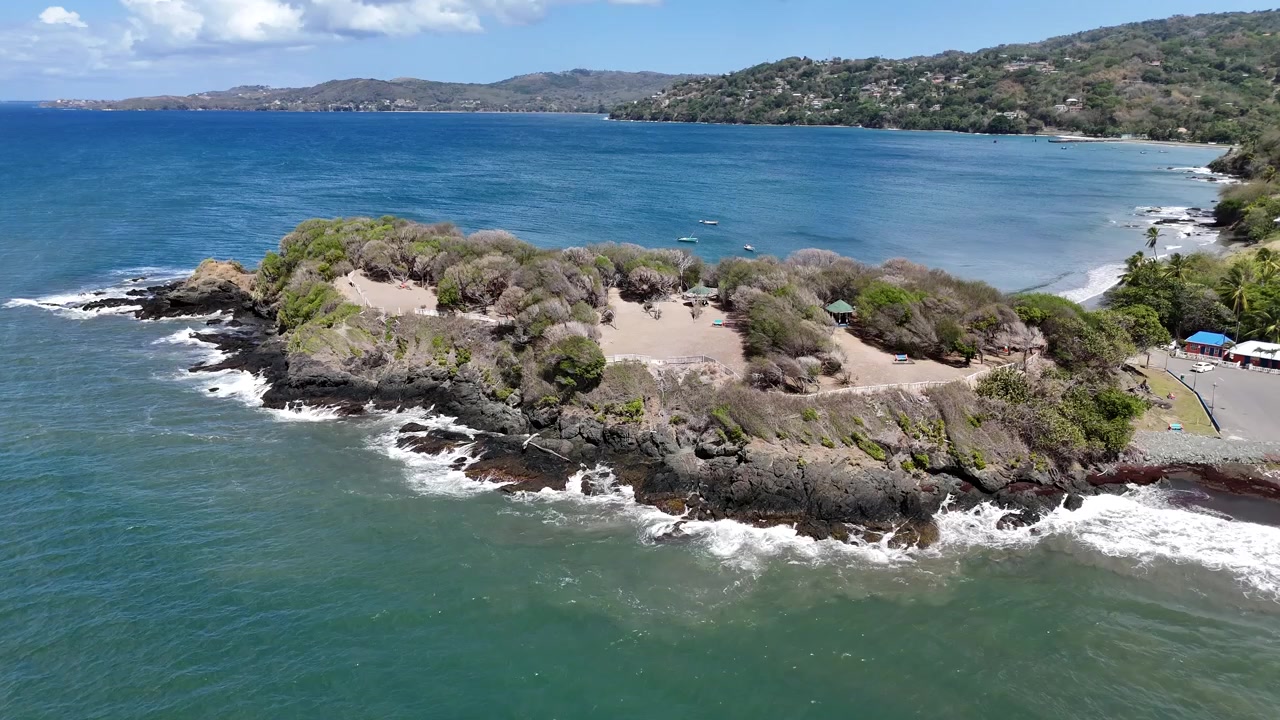 Drönare som cirkulerar runt den klippiga udden vid Granby Fort. Turkosfärgat karibiskt vatten virvlar runt de vulkaniska klipporna på Tobago Island under en klar himmel i Trinidad och Tobago