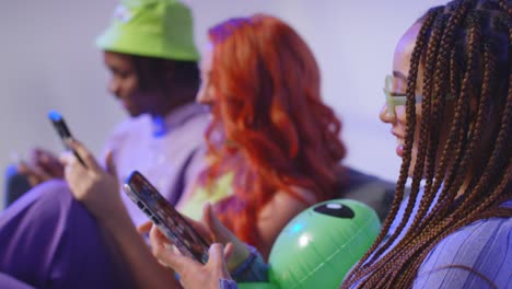 close up studio shot of young gen z friends sitting on sofa talking and sharing social media post on mobile phones 2