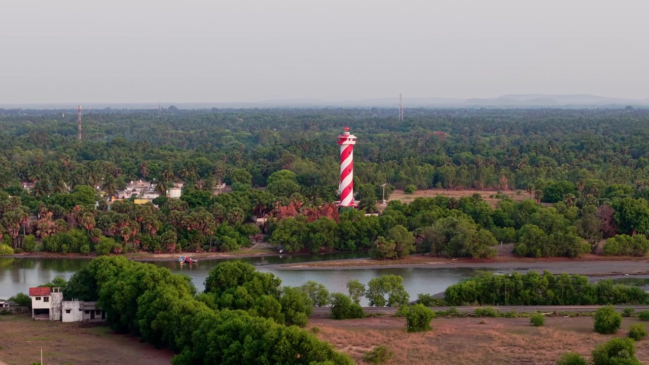 Luftfoto fra drone af rødt og hvidt stribet fyrtårn med udsigt over bagvande, flod og frodigt kystlandskab nær Chennai i Tamil Nadu, Indien