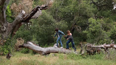 a hispanic couple walks on a fallen tree branch in a park laughing and enjoying each others company