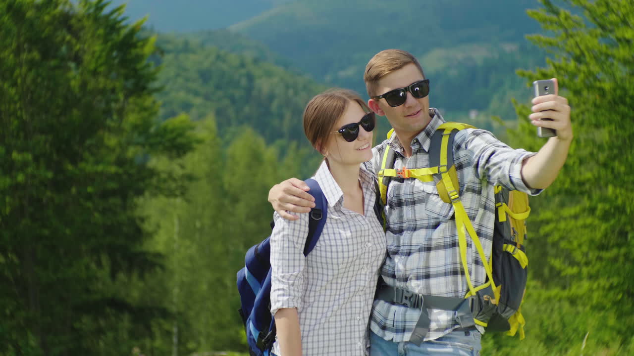 una pareja joven de turistas con mochilas se toman fotos con un teléfono inteligente en una hermosa