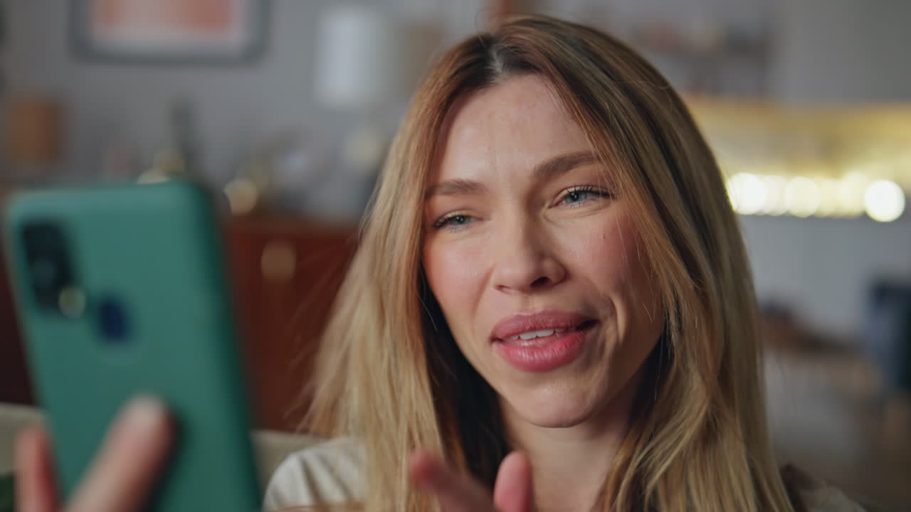 Emotional girl videocalling boyfriend holding mobile phone at home close up.