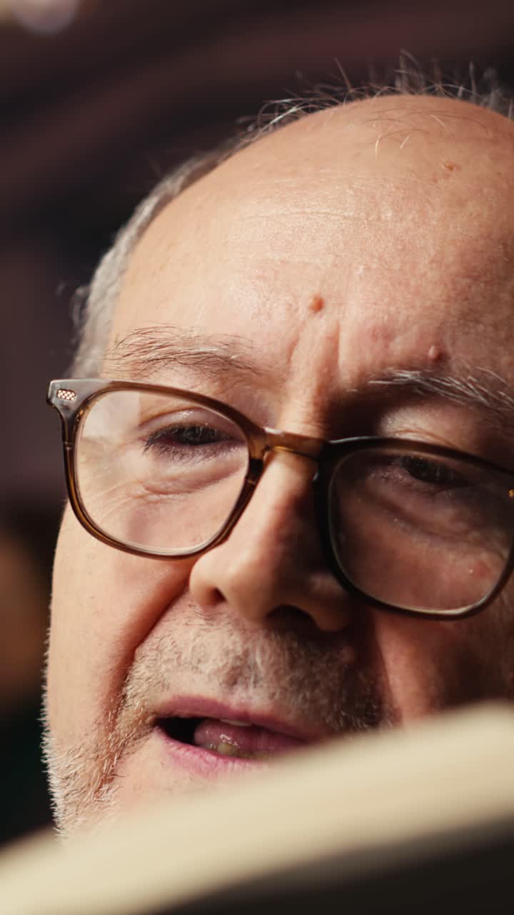 Vertical Video Old person with spectacles enjoys reading a book at the library