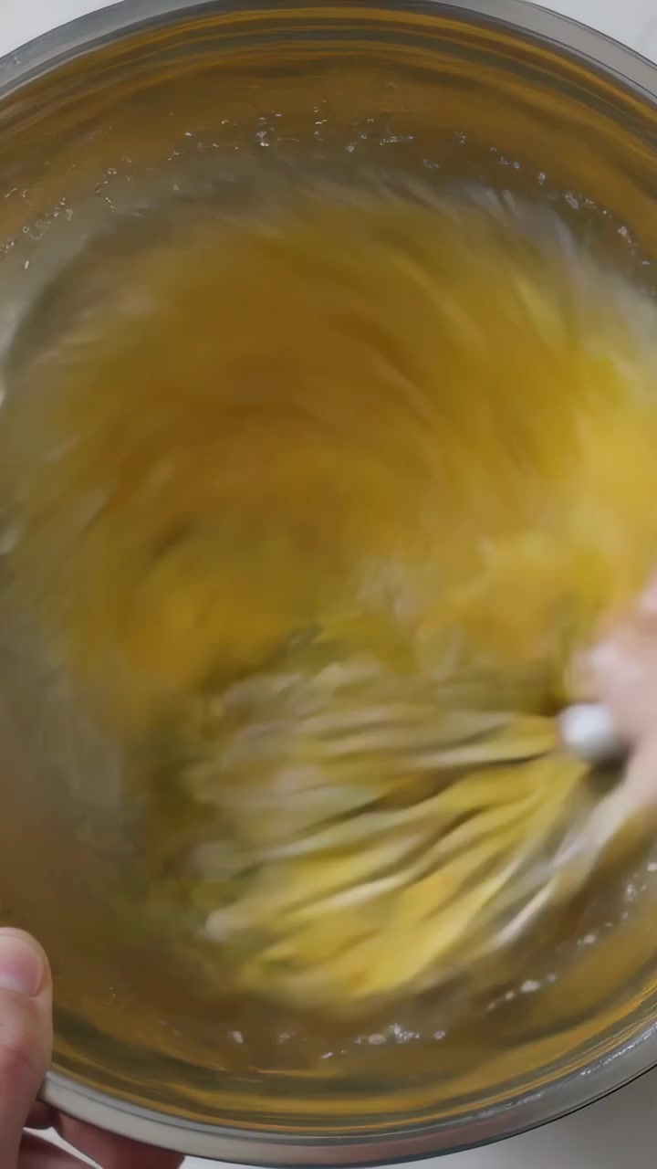 Video verticale: Mani che mescolano portando una frusta in una ciotola sul bancone della cucina, sbattendo le uova per cucinare