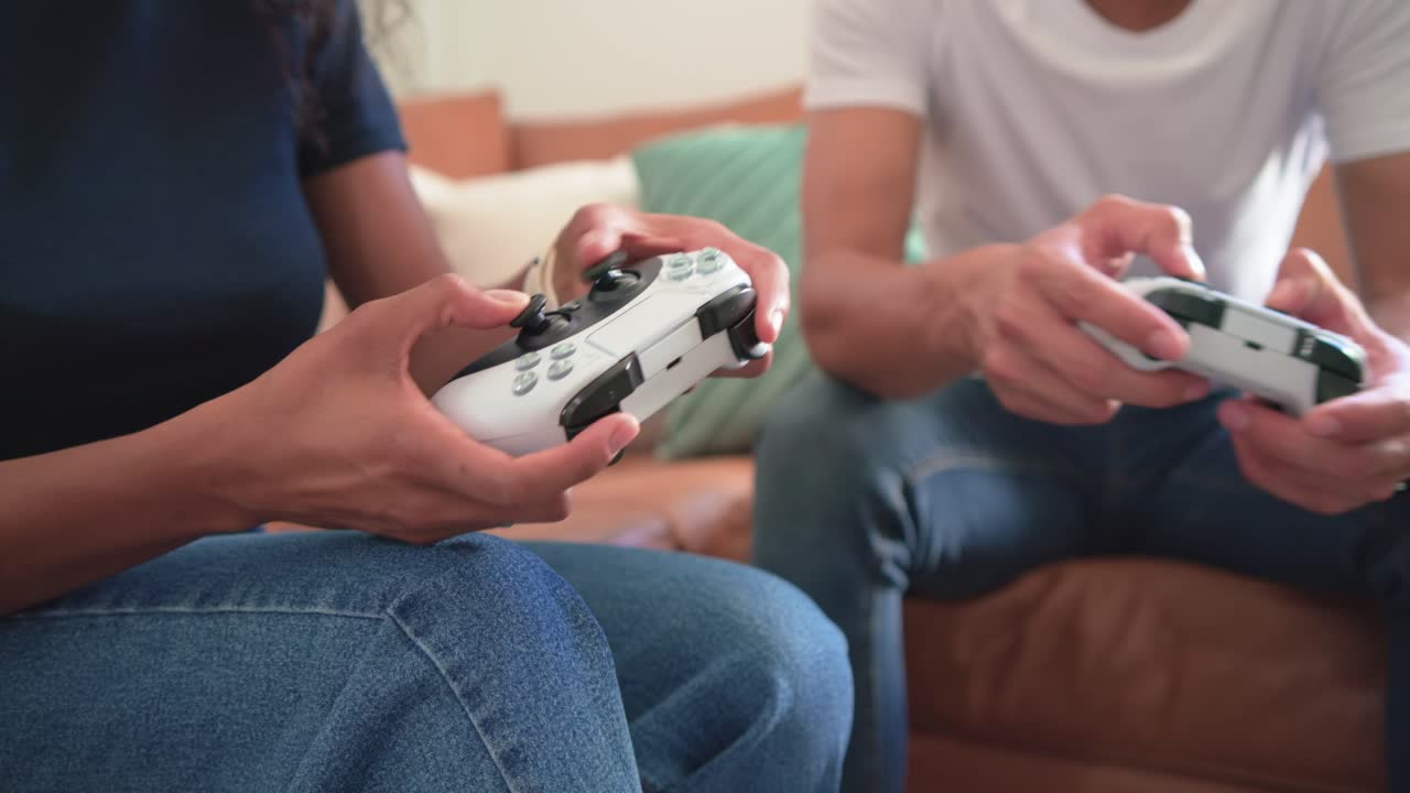 ソファでゲーム中のアフリカ系アメリカ人カップルが、コントローラーのグリップを調整している。