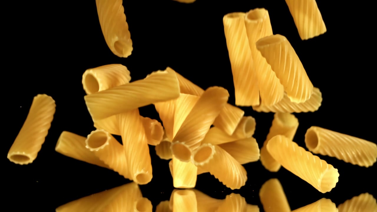 Rigatoni secchi che cadono al rallentatore su sfondo nero
