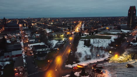 Aerial-drone-shot-of-cityscape,-trucks-driving-and-clearing-snow-after-a-snowstorm---drone-view-dolly-shot