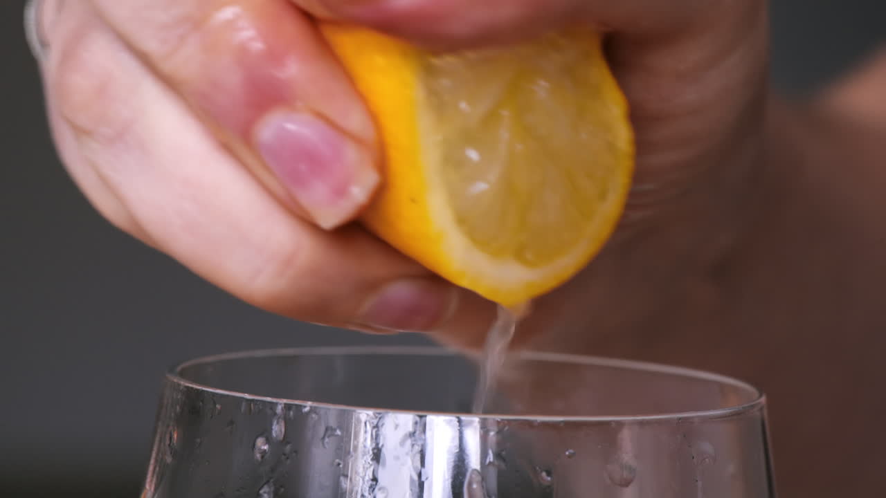 A woman squeezes juice from a lemon into a glass. Slow motion