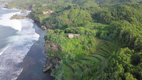 Toma-Aérea-De-Interés-De-Las-Olas-Que-Llegan-A-La-Costa-Verde-De-Indonesia-Con-Casa-Privada-En-El-Acantilado