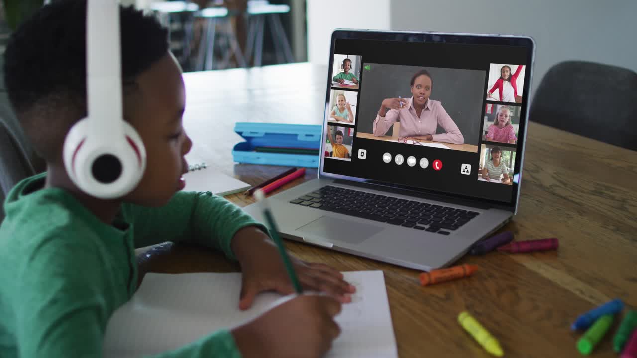 Schoolboy using laptop for online lesson at home, with diverse teacher and class on screen