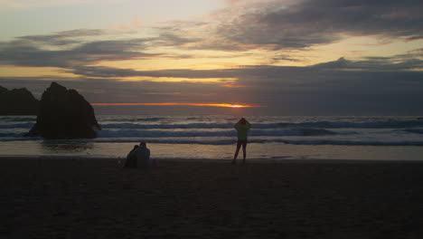 dramatic sunset over holywell bay beach with people on the sandy seashore in cornwall, england. static shot