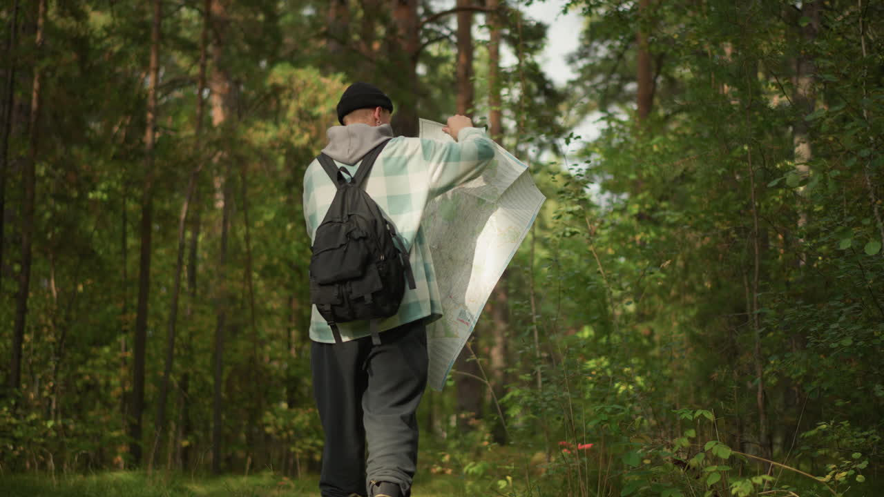 Escursionista caucasico che apre una mappa nella foresta, spiegando un'ampia mappa di carta come un mantello mentre si ferma su un sentiero di pini illuminato dal sole, indossa un berretto e uno zaino, una leggera brezza muove le foglie, atmosfera di scoperta giocosa