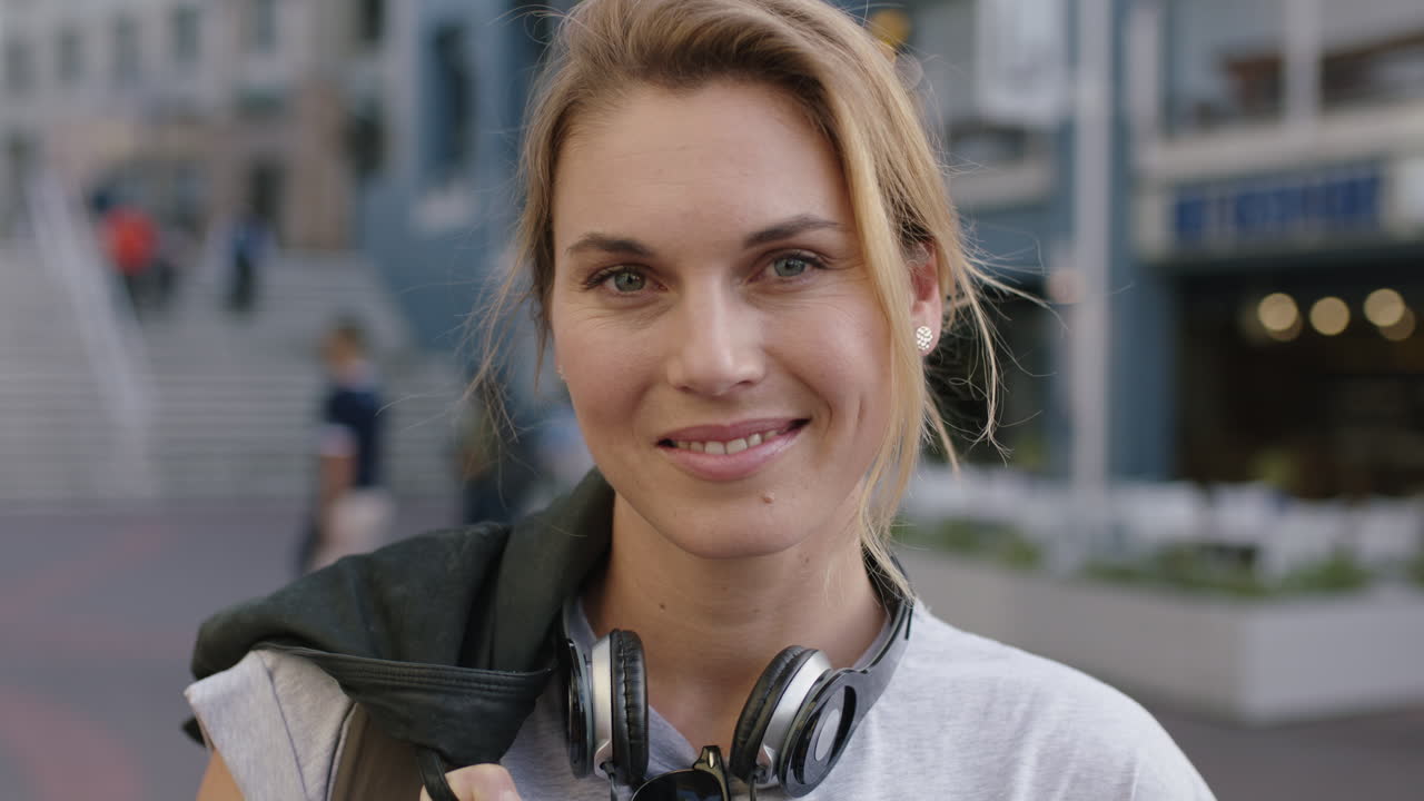 retrato de una mujer rubia independiente sonriendo feliz optimista con auriculares en la acera de la ciudad urbana