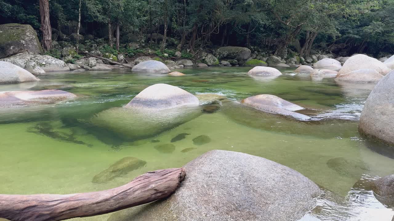A tranquil river flows over smooth rocks in a lush rainforest setting, with gentle lighting and a peaceful atmosphere