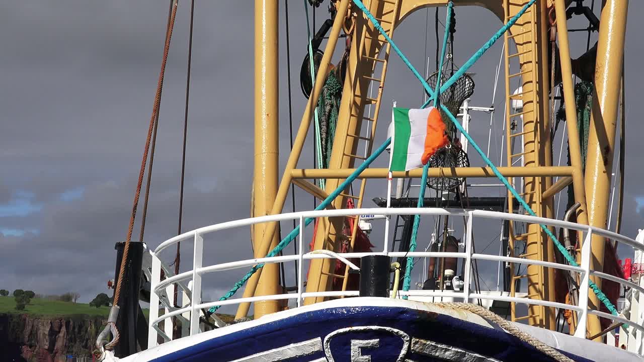 Dunmore East Waterford trawler in port with grey storm clouds and an Irish flag fluttering in the high winds of a winter storm