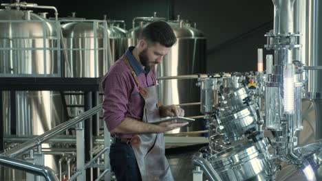 un joven cervecero con un delantal de cuero supervisa el proceso de fermentación de la cerveza en una fábrica de cerveza moderna