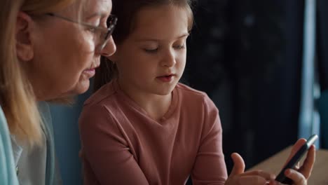 side view of caucasian grandmother teaching granddaughter how to use  mobile phone in the kitchen