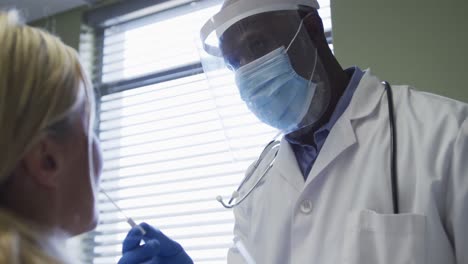 Diverse-female-patient-and-doctor-wearing-face-mask-doing-covid-swab-test