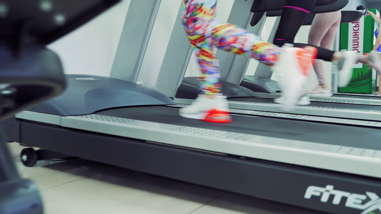Close-up of women's legs in sport trainers running on the treadmills in a new gym. Fitness and healthy lifestyle concept.