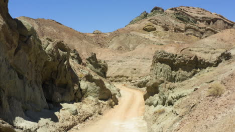 slowly travelling down a curving dirt road slicing between two large rock formations in the mojave desert