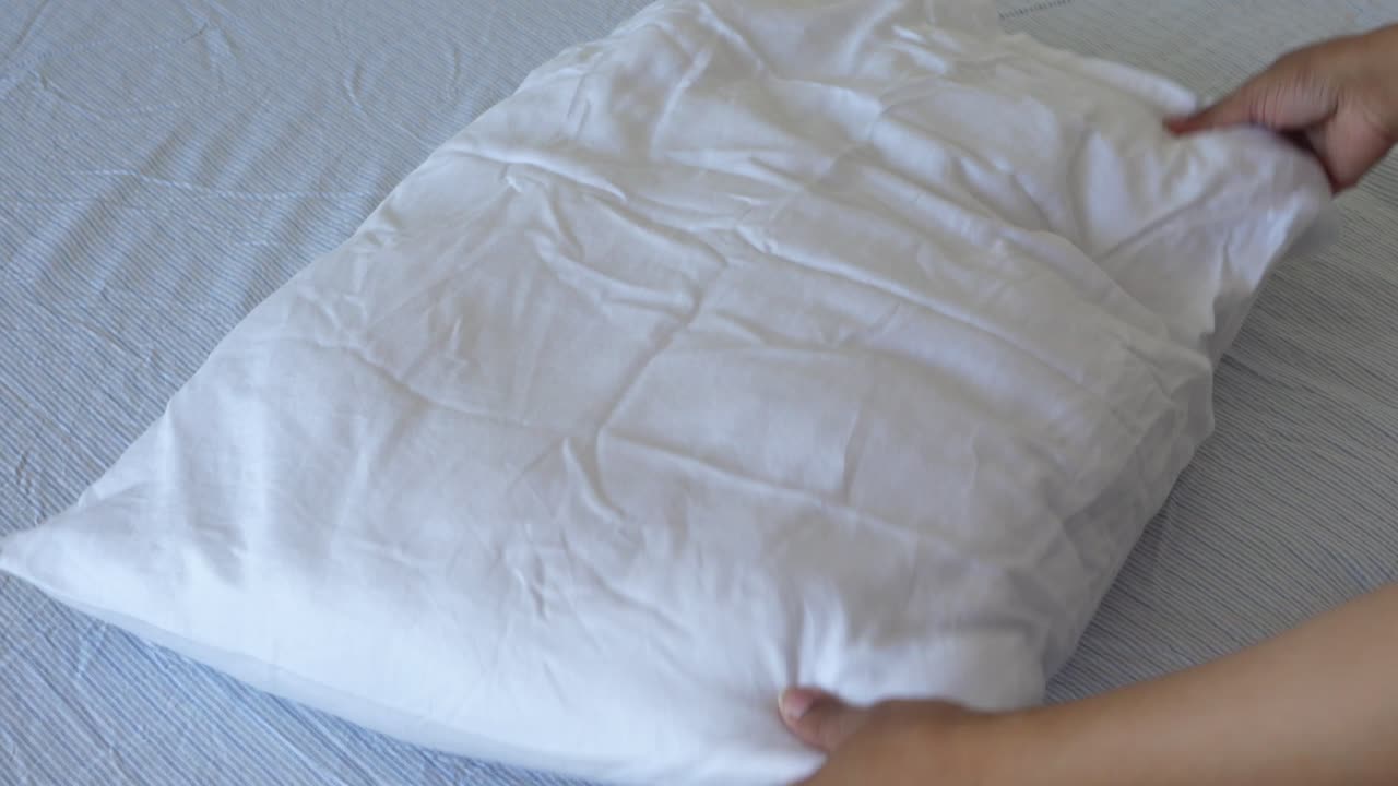 Woman arranging a white pillow on a bed