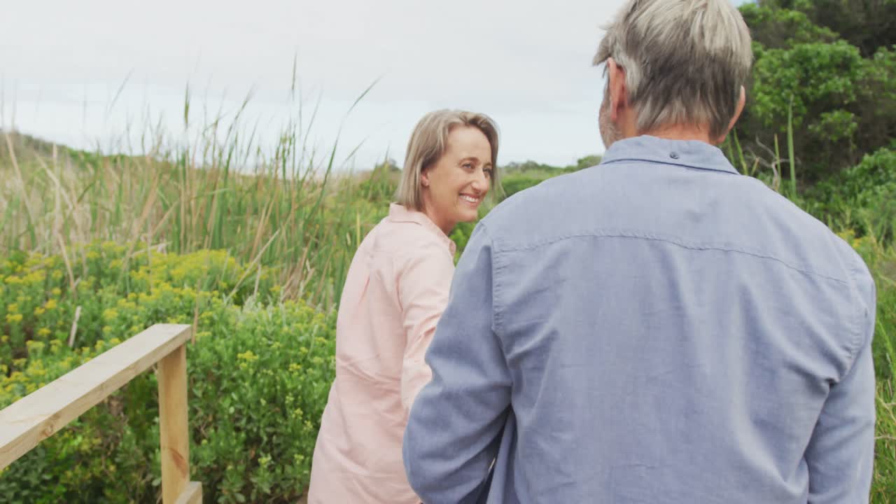 웃는 고위 백인 커플이 손을 잡고 야외의 길을  ⁇ 고 있습니다.