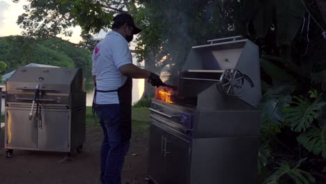 Parrilla-Mexicana-Latina-Taquero-Parrilla-Barbacoa-Con-Llamas-En-La-Parrilla-Preparando-Carne-De-Bistec-Cruda-En-El-Servicio-De-Fiesta-Al-Atardecer-Del-Lago-Jardín