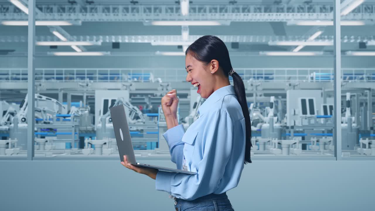 Woman celebrating success in modern factory using a laptop