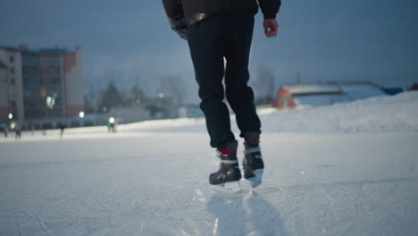 skaters gliding on ice rink under bright artificial lights during cold winter evening focus on lower body in black skating boots visible textured surface with blurred skater and buildings