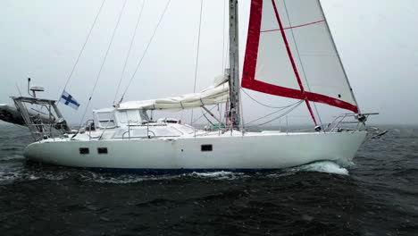 White-sailboat,-sailing-during-a-snowstorm-on-the-open-sea---Aerial-view