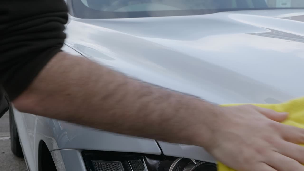 Medium shot removing polish from a white car hood with a yellow microfibre cloth towel